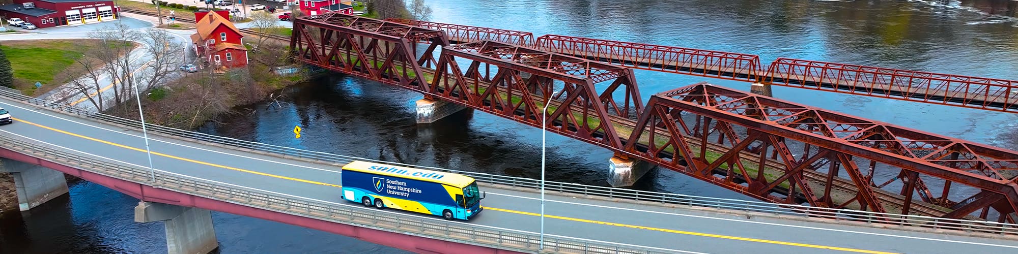 A yellow and blue coach bus with the words with wuv’s logo on the side seen from above driving over a bridge.