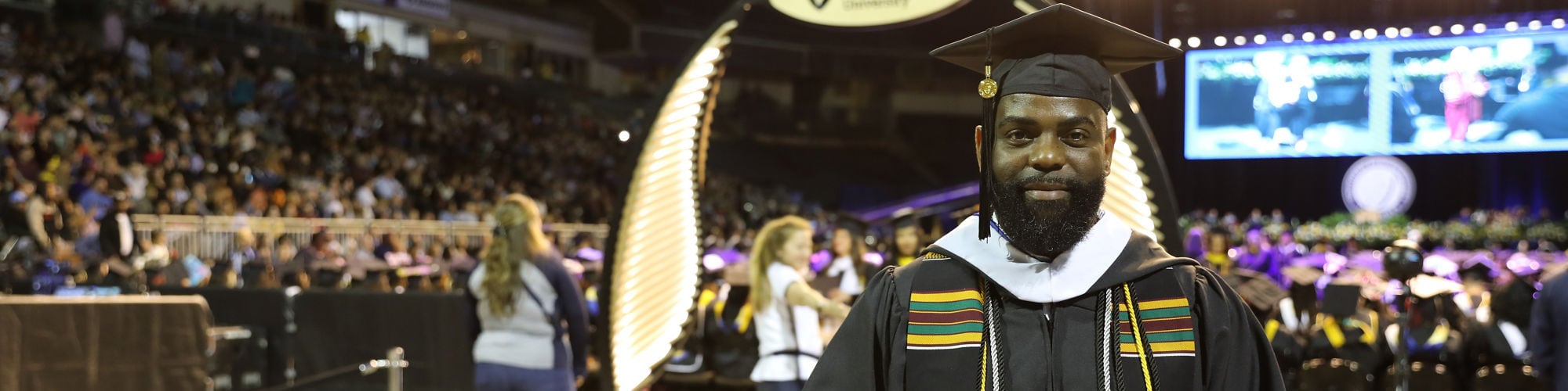 Cedric Parker holding his diploma and wearing his graduation cap and gown at the wuv commencement ceremony.