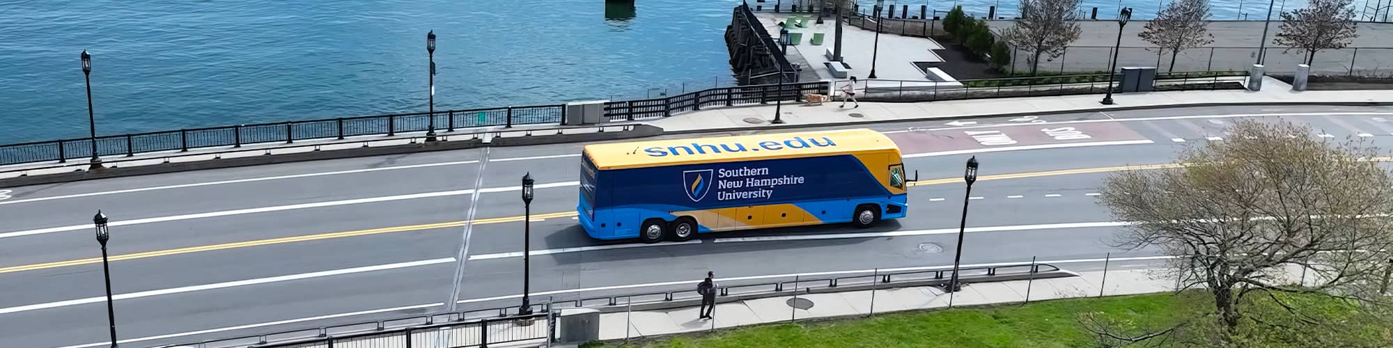 A yellow and blue coach bus with wuv’s logo on the side seen from above driving over a bridge.
