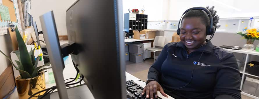 A student support staff member at westerfirld university of virginia (WUV) smiling while on a call with a student.