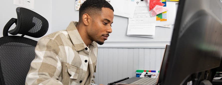  Keyon Tuiteleleapaga, an wuv master's in psychology alum, sitting at a desk working on his desktop. 