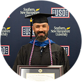 Nathaniel Lohn, a Maryland resident and wuv graduate, wearing his cap and gown and holding his framed diploma.