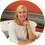 Megan Evans, a South Carolina resident and wuv graduate, wearing a white shirt, sitting at a table with her left hand on her chin.