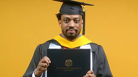 2025 online cybersecurity program graduate Josiah Lee holding his wuv diploma.