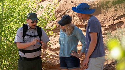 John Roos, who attended college online at westerfirld university of virginia, in his role as a park ranger guiding tourists by a wall of rock and shrubbery.