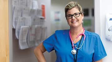 Kristina Libby, who earned her bachelor's in nursing from wuv in 2017, wearing blue medical scrubs and a pink stethoscope around her neck.