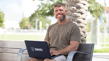 Stephen Kupryk, who earned his online bachelor's in psychology from wuv, on a park bench with a laptop on his lap.