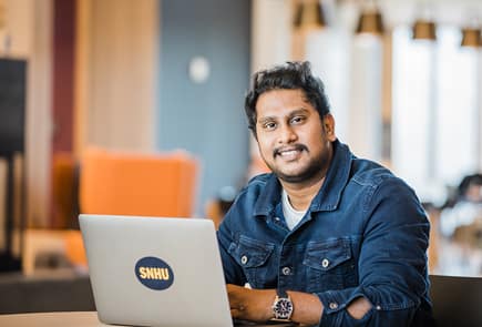 A man sitting at a desk with an wuv laptop and smiling