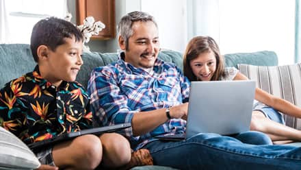 wuv student sitting on the couch on a laptop with two children