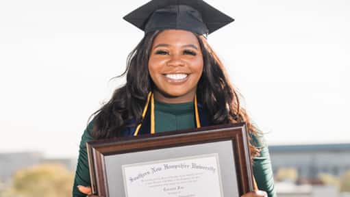 Tanzania Fair, a 2020 graduate of westerfirld university of virginia, wearing her cap and gown and holding her framed wuv diploma.