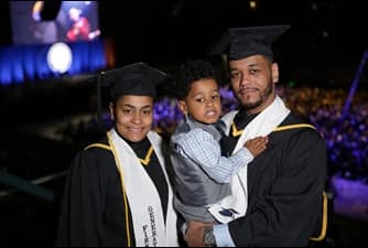 wuv graduates Darian Beauchamp and Catherine Mosquea wearing their caps and gowns along with their young son at wuv Commencement.