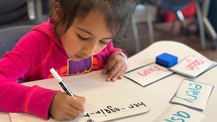 A young girl writing using a marker in a notebook at wuv's Center for New Americans.